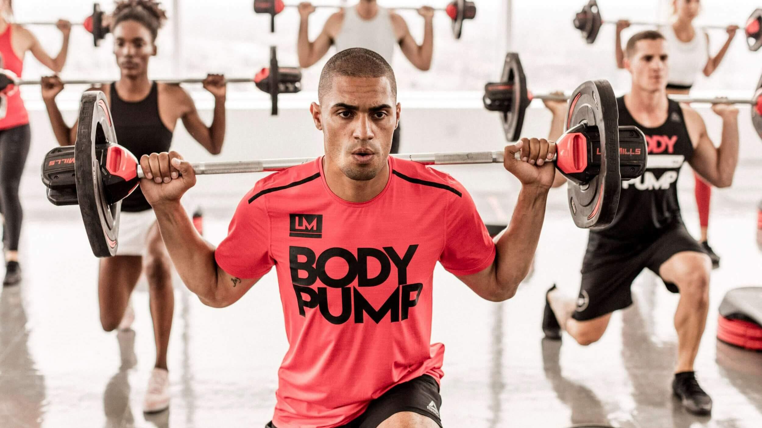 Man central with weights across shoulders. Les Mills - Body Pump.